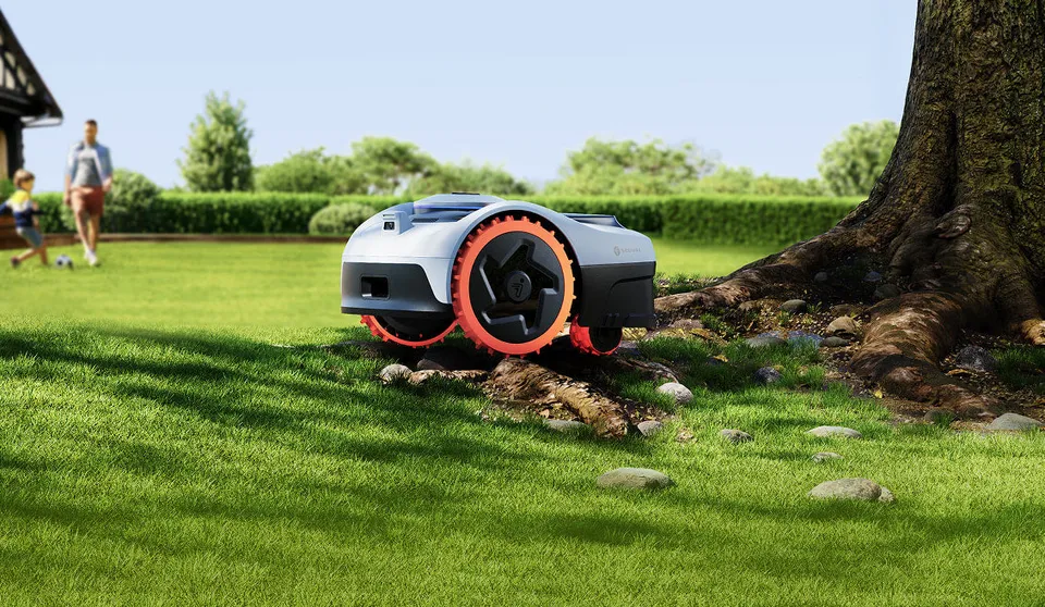Navimow i2 AWD robot mower on a lawn at the foot of a tree with exposed roots, while a family plays football at the end of the garden